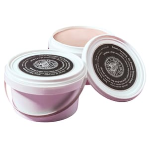 White and pink containers of body cream with tribal chocolate branding, featuring a dark circular label on the lid with text and a logo.