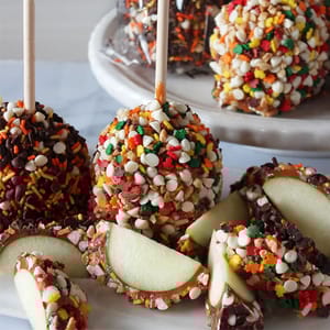 Caramel apples coated in various colorful sprinkles and chocolate chips, with some sliced to show the interior.