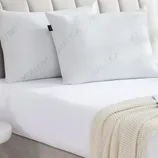 Two white pillows with the brand name \“Nautica\“ embossed on them are placed on a bed with a white sheet and a cream-colored knitted throw.