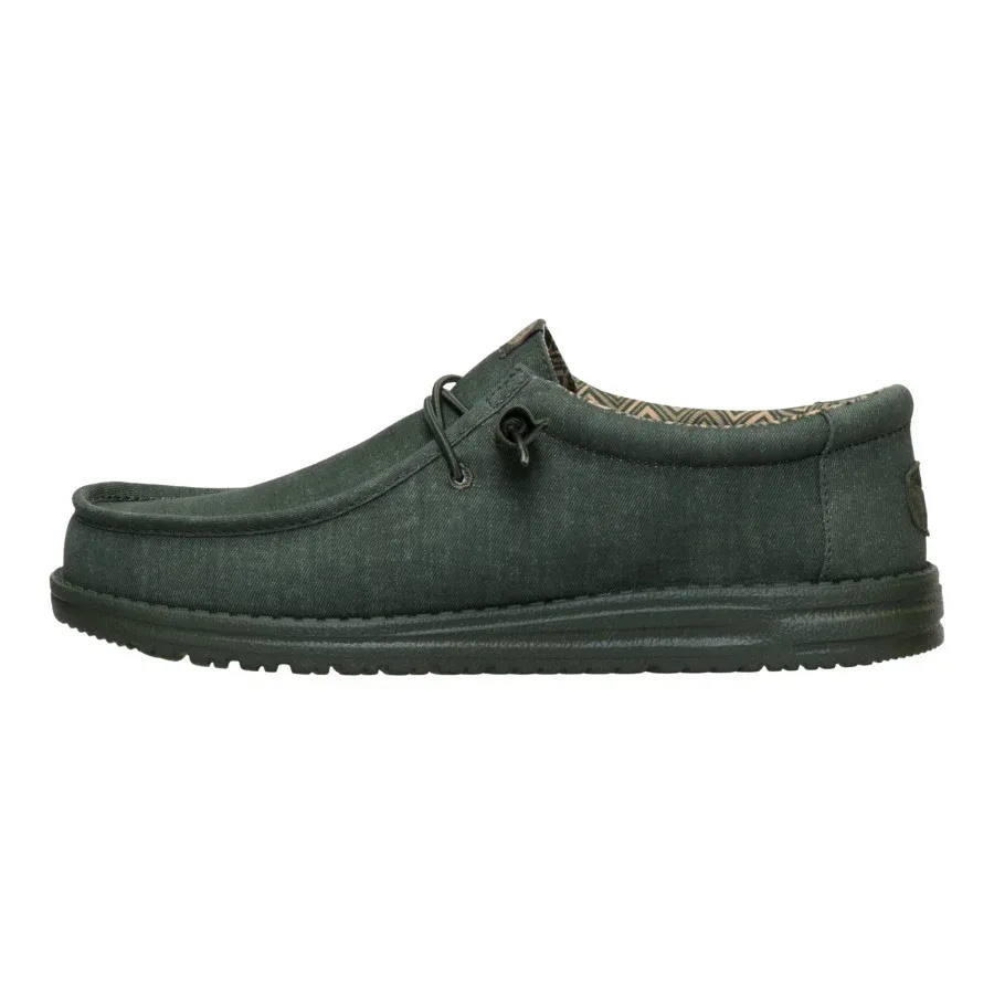 A casual, dark green slip-on shoe with a textured sole and patterned interior, featuring a moccasin-style design and lace accents.