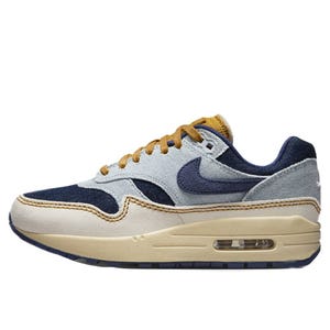A sneaker with a combination of denim and suede textures in blue, gray, and beige tones, featuring a visible air unit in the sole.