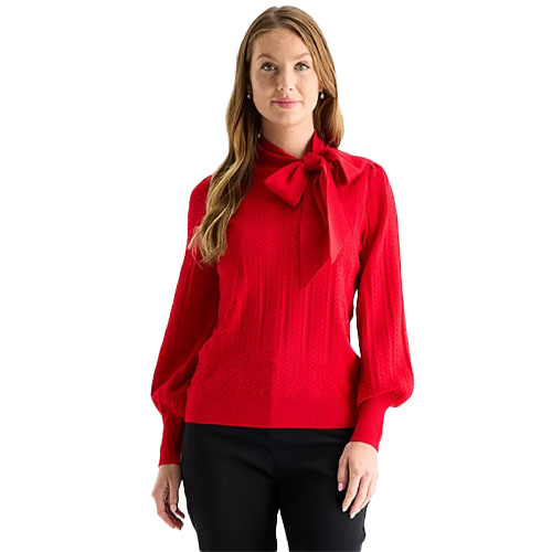 A woman is wearing a red sweater with a large bow tie at the neck and long sleeves, paired with black pants.