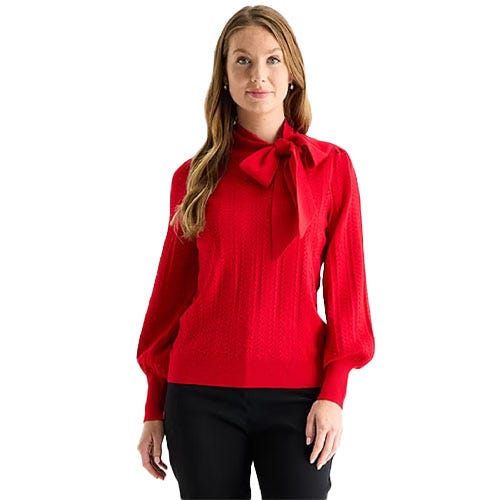 A woman is wearing a red sweater with a large bow tie at the neck and long sleeves, paired with black pants.
