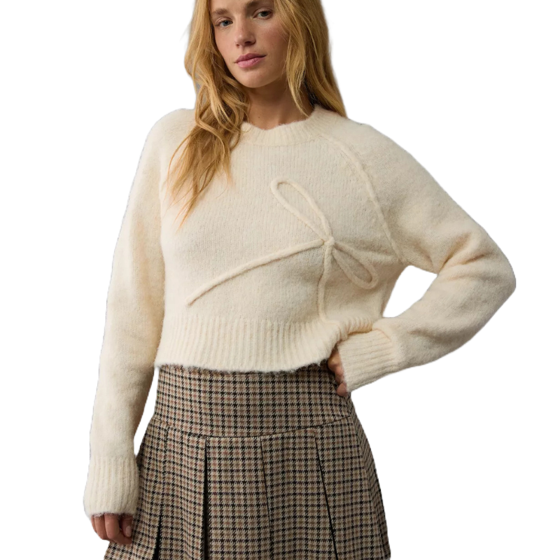 Cream-colored, cropped crew neck sweater with a decorative bow detail on the front, paired with a pleated plaid skirt.