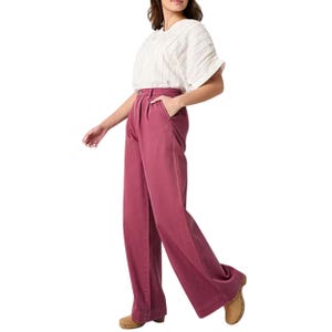 A woman is wearing high-waisted, wide-leg rose-colored pants paired with a white short-sleeve striped top and tan shoes.