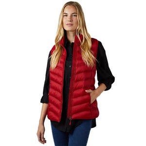 A woman is wearing a red puffer vest over a black long-sleeve shirt and blue jeans.