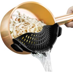 A black clip-on pot strainer is attached to a copper pot, draining water from cooked noodles.