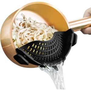 A black clip-on pot strainer is attached to a copper pot, draining water from cooked noodles.