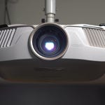 A mounted white projector with a large lens emitting a blue light.