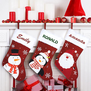 Three Christmas stockings hanging on a mantel, each with a white top. They feature a snowman, a penguin, and Santa Claus design, labeled \“Emily,\“ \“Ronald,\“ and \“Amanda.\“ The mantel is decorated with red and white candles, ornaments, and small gift boxes.