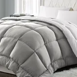 A gray, quilted comforter with a plush, diamond-pattern design is placed on a bed with white pillows and sheets.