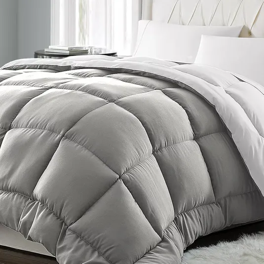 A gray, quilted comforter with a plush, diamond-pattern design is placed on a bed with white pillows and sheets.