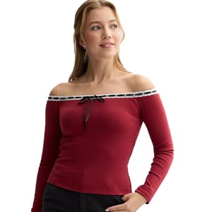 A woman wears a Madden Girl off-the-shoulder top, featuring a red long sleeve design with a black ribbon detail and a white lace trim at the neckline.