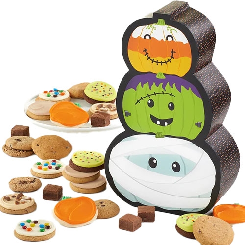 Halloween-themed gift box with three stacked monster faces, surrounded by a variety of cookies and small brownies, including frosted and chocolate chip options.