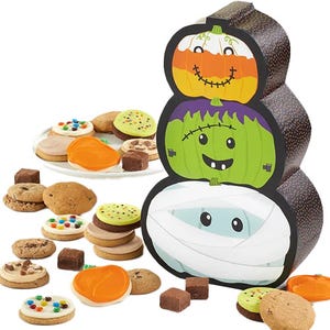 Halloween-themed gift box with three stacked monster faces, surrounded by a variety of cookies and small brownies, including frosted and chocolate chip options.