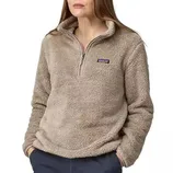 A woman is wearing a beige, plush half-zip fleece pullover with a small brand logo on the chest, paired with dark pants.