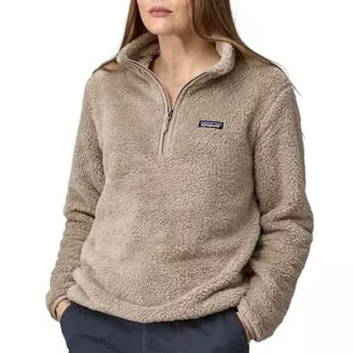 A woman is wearing a beige, plush half-zip fleece pullover with a small brand logo on the chest, paired with dark pants.