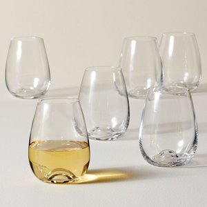 A set of six clear, stemless wine glasses with a rounded shape and a slightly indented bottom for easy grip, one filled with a light-colored liquid.