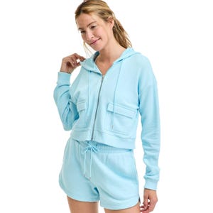 A woman is wearing a light blue hooded sweatshirt and matching drawstring shorts, both with a casual, relaxed fit.