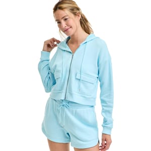 A woman is wearing a light blue hooded sweatshirt and matching drawstring shorts, both with a casual, relaxed fit.