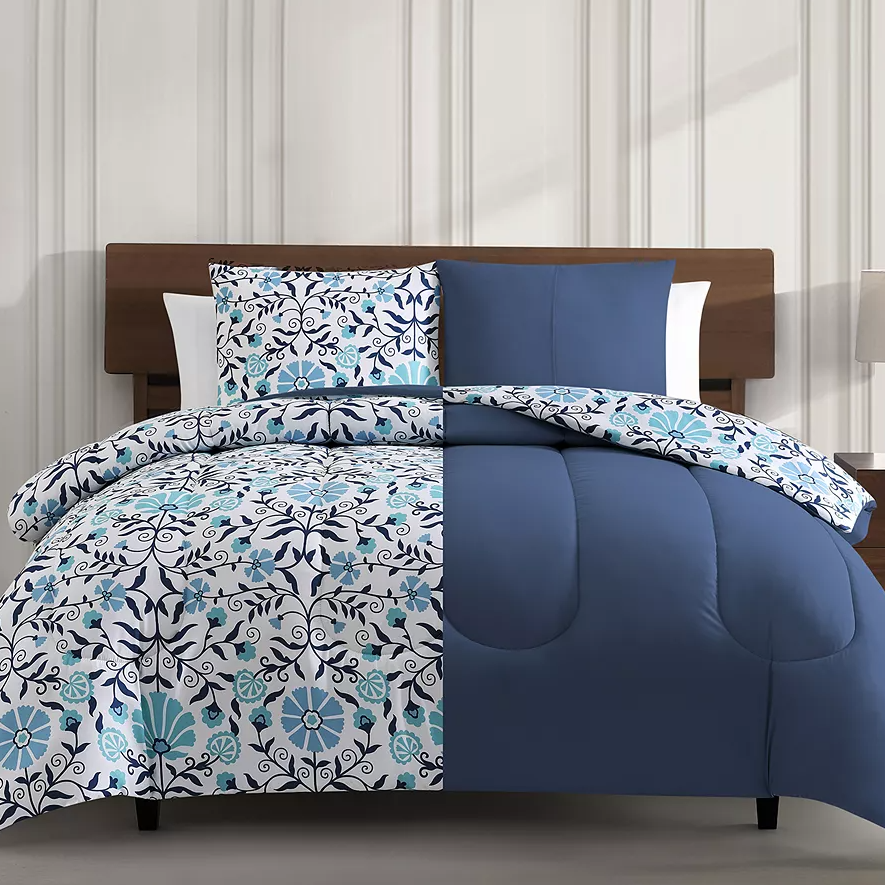 A bedding set with a floral pattern in blue and white tones, including a comforter and pillow shams on a bed.