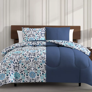 A bedding set with a floral pattern in blue and white tones, including a comforter and pillow shams on a bed.