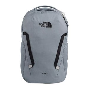 A grey North Face Vault backpack with a front zipper compartment and two side pockets, featuring black adjustable shoulder straps and logo branding.