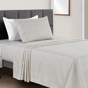 A neatly made bed features a light-colored sheet set with a subtle geometric pattern, accompanied by matching pillowcases and a contrasting white pillow. The headboard is upholstered in dark gray fabric.