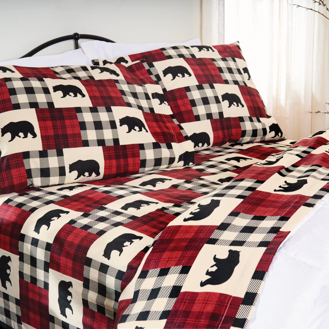A flannel sheet set featuring a red and black plaid pattern with silhouetted black bears. It includes pillowcases and a fitted sheet, creating a rustic and cozy design for bedding.