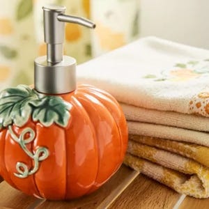 A pumpkin-shaped soap dispenser paired with folded, patterned towels on a wooden surface.