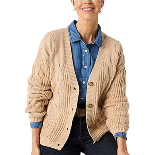 A woman wears a beige cable-knit cardigan over a denim button-up shirt, paired with dark jeans.