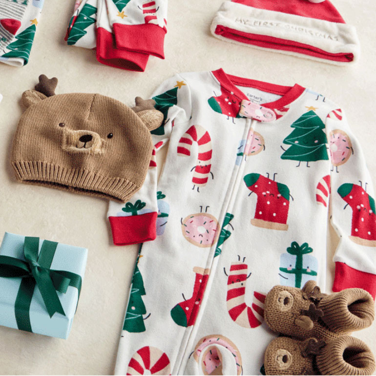Baby Christmas-themed clothing set includes a zip-up onesie with festive prints, a reindeer knit hat, a Santa hat labeled \“My First Christmas,\“ and matching booties, accompanied by a small gift box wrapped with a green ribbon.