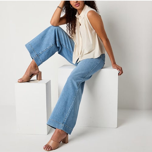 A woman models wide-leg blue jeans, a sleeveless cream blouse, and brown strappy heels.