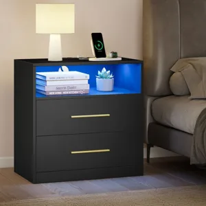 A black nightstand with a blue-lit open shelf, two drawers with gold handles, a lamp, and a charging phone and watch. Branded with \“VASAGLE by SONGMICS HOME.\“