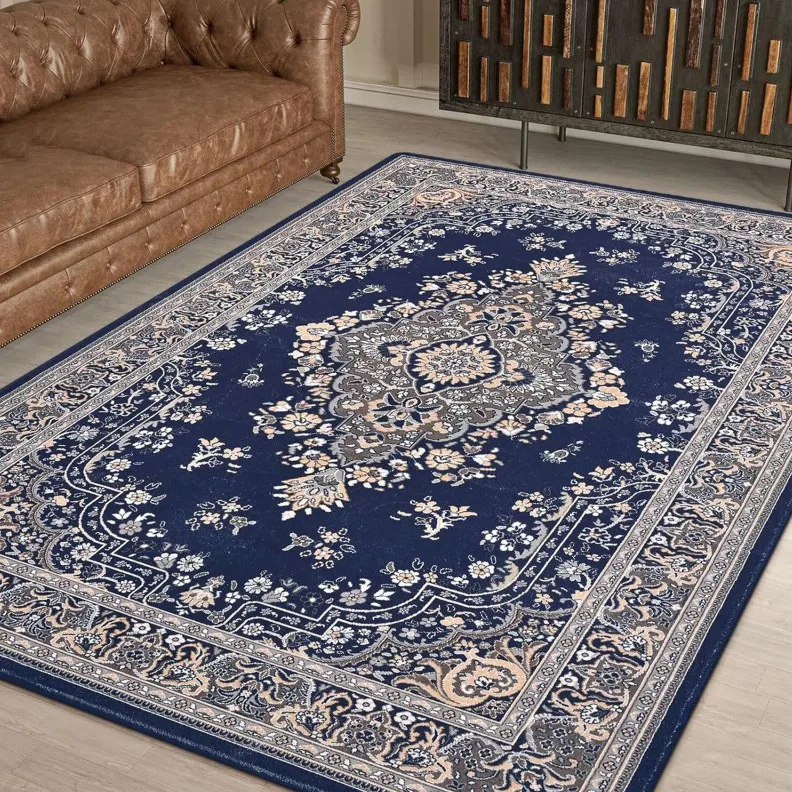 A blue Persian-style rug with intricate floral patterns, placed on a wooden floor, next to a brown tufted leather sofa.
