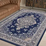 A blue Persian-style rug with intricate floral patterns, placed on a wooden floor, next to a brown tufted leather sofa.