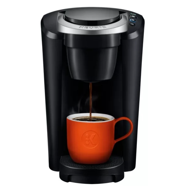 A black single-serve coffee maker brews into an orange mug positioned on its tray.