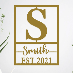 Wall decor featuring a large letter \“S,\“ the name \“Smith,\“ and \“EST 2021,\“ with a minimalist design accompanied by plants on either side.