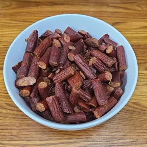 A bowl filled with small, dark brown pieces resembling chopped smoked sausages, placed on a wooden surface.