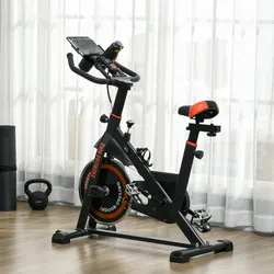 Indoor exercise bike with adjustable seat and handlebars, featuring a flywheel marked \“EXERCISE BIKE\“ and \“INDOOR CYCLING,\“ a tablet holder, and a water bottle holder. Nearby are a yoga mat and a kettlebell.
