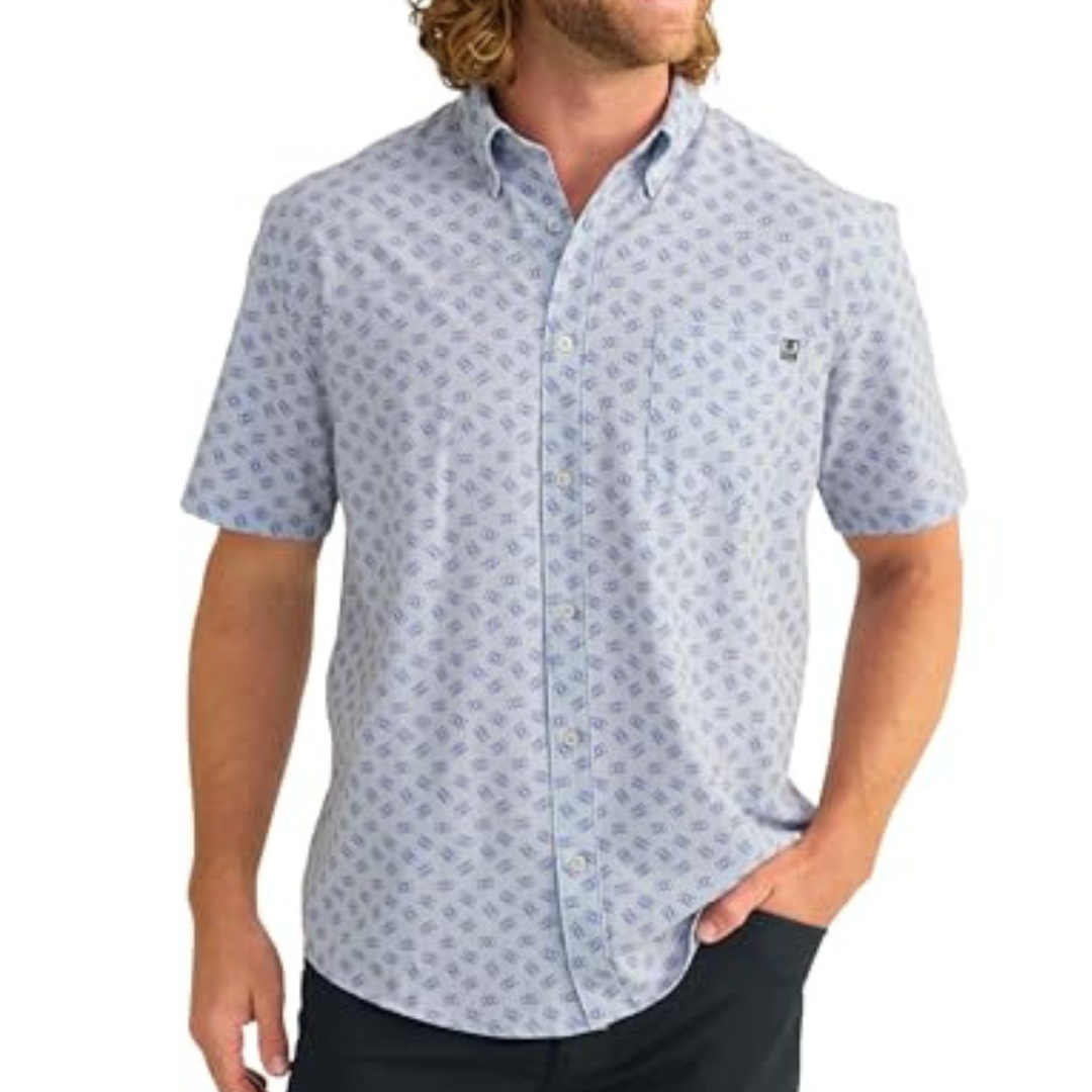 A man is wearing a short-sleeve, light-blue button-up shirt with a small geometric pattern, paired with dark pants.