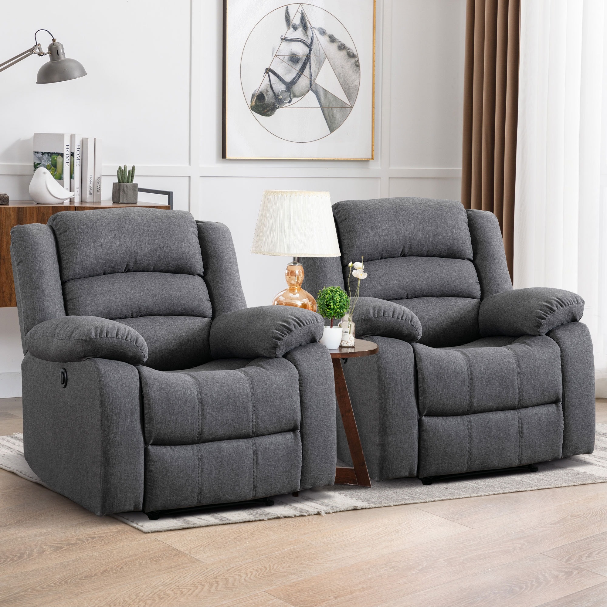 Two gray recliner chairs are placed side by side with a small table in between, featuring a lamp and potted plants.