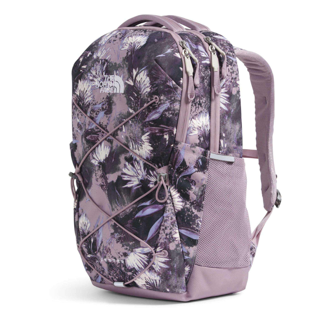 A floral-patterned North Face backpack with dual zippers, a front bungee cord system, and side mesh pockets, primarily in shades of purple.