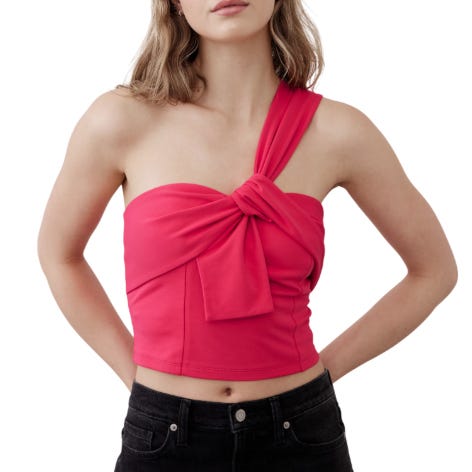 A woman wearing a one-shoulder, hot pink crop top with a twist knot detail, paired with black jeans.