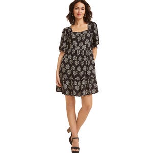 Woman wearing a black dress with a white floral pattern, featuring a square neckline, puff sleeves, and a knee-length hem, paired with black sandals.