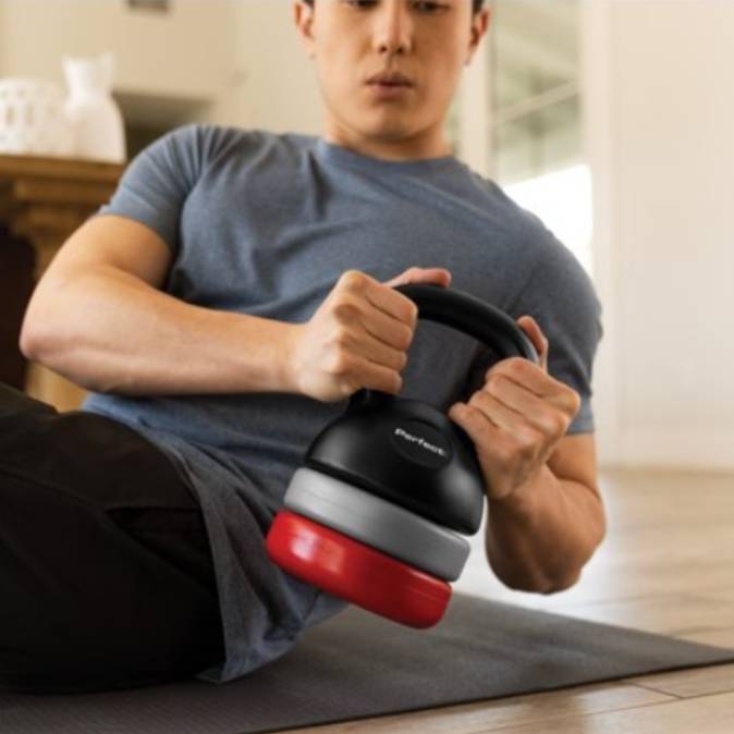 A man is using a black and red adjustable kettlebell for a workout.