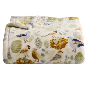 A folded, plush blanket features a whimsical pattern of birds, nests, and foliage in soft, natural colors.