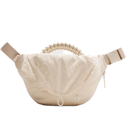 A beige, crossbody-style belt bag with a gathered elastic handle and adjustable strap, featuring a zipper closure and a small emblem.