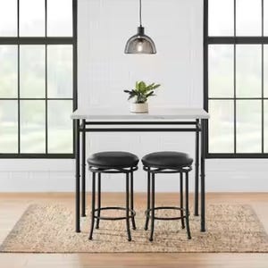 A modern bar table with two stools and a hanging industrial-style pendant lamp above it.