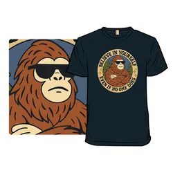 A black t-shirt features a graphic of a cool Bigfoot wearing sunglasses with the text \“Believe in yourself even if no one does\“ surrounding the image.